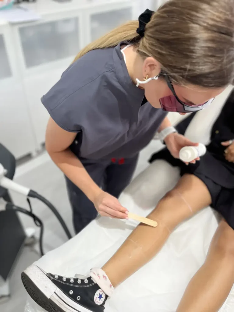 Aesthetic practitioner applying soothing gel to a client's leg with a wooden spatula before a laser hair removal procedure.